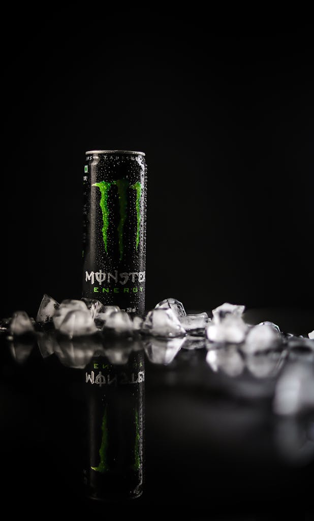Artistic photo of a chilled energy drink can surrounded by ice cubes on a reflective black surface.